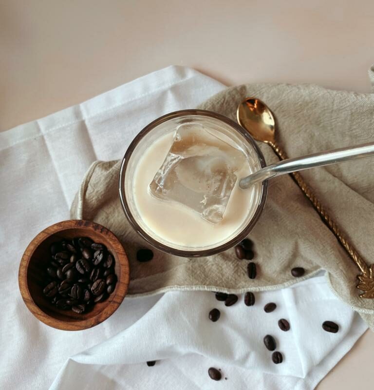 Glass of iced coffee with straw and coffee beans in a bowl on the left hand side.