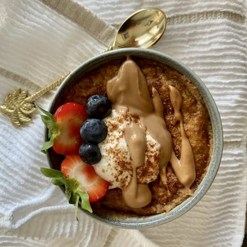 Bowl of Chocolate Banana Baked Oats on white tea towel and gold spoon