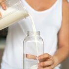 Woman pouring freshly made plant based milk into a clear glass bottle