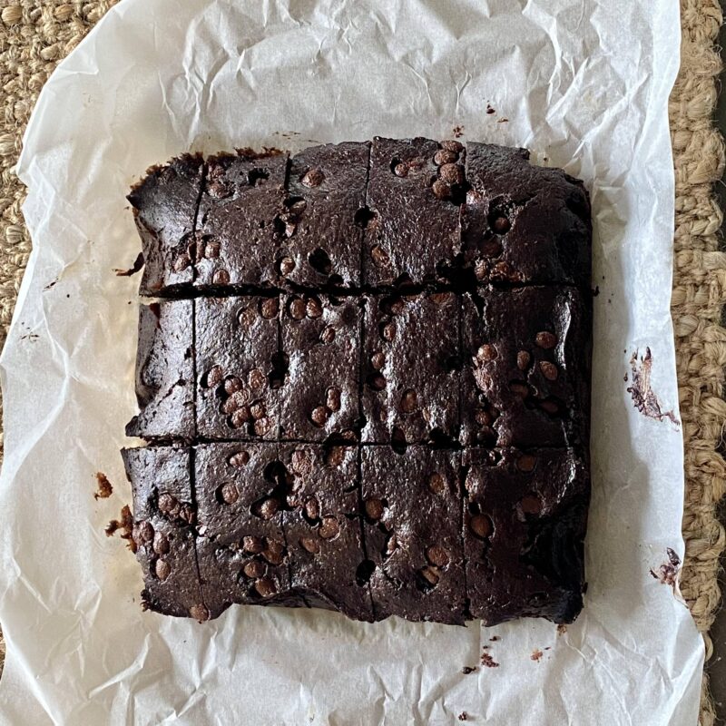 Dark brown chocolate vegan brownie on white baking paper. Brownie is sliced into 12 pieces.