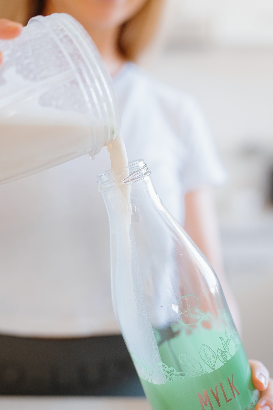 Woman pouring freshly made milk into glass bottle.