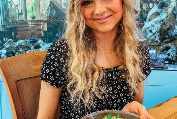 Woman with long blonde hair, sitting down and smiling with a healthy bowl of vegetables